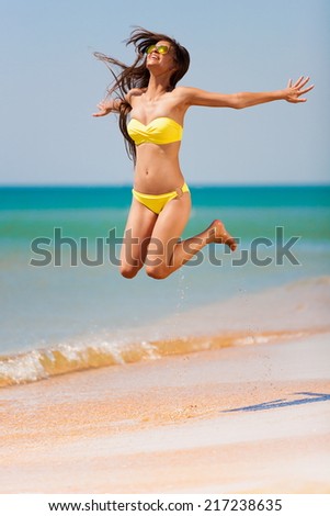 beautiful fun and joy brunette smiling woman in yellow bikini jump  tropical  blue sea water has sports and tan body