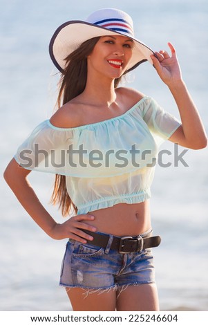 beautiful  brunette  sexy  smiling  woman in blue jeans shorts, blouse and white hat in sea water background have  tan skin, red lips  and sport  body