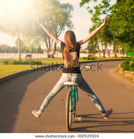 Beautiful sensuality elegance red hair back woman cyclist, has black shirt, blue jeans. Has slim sport body and ass. Motion on great bicycle in urban city. Portrait nature amazing sunset.