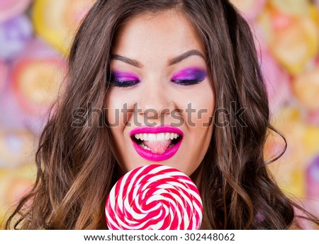 Beautiful amazing sexy elegance lady brunette woman, has joy fun smiling tan face, brown eyes, white teeth,  pink makeup, eating lollipop. Studio portrait. Lipstick