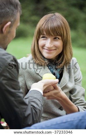 man gives apple to woman in a city park
