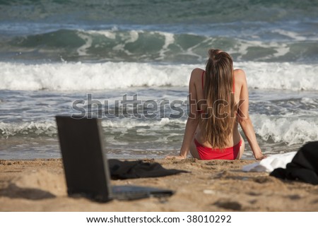 woman in bikinis sitting on the beach - laptop, jacket and blouse lying in sand