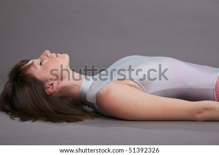 young woman in silver leotard with closed eyes doing breathing exercises on the ground