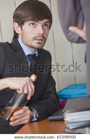 office scene - businessman hiding a bottle of alcohol under the desk