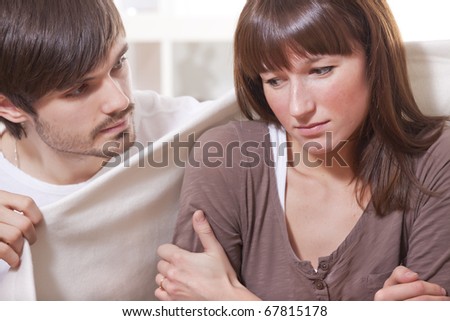 young man covering ill woman with rug at home