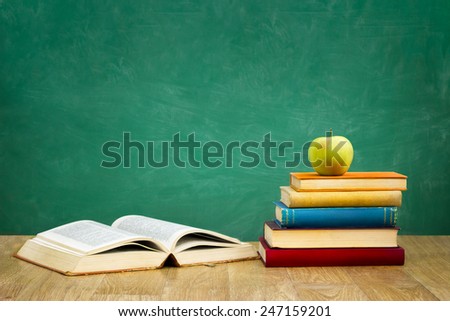 pile of books with one book open on empty green  school board background