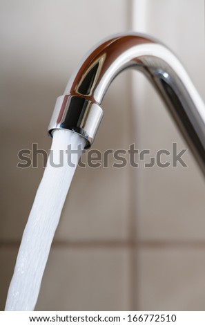 Vertical image of a tap with water flowing strongly under high pressure