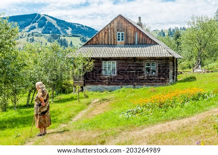 SLAVSKA/UKRAINE - JULY 27, 2007 - An elderly woman with a cane stands on the path to the background of the old wooden houses and mountains Trostyan Slavskoe resort, Carpathians.