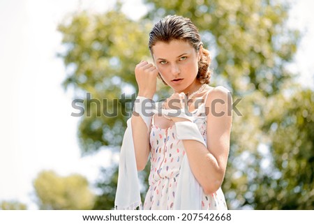 A pretty young woman is playing with a scarf in the park, the strong summer sun lights her in back light.