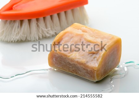 A piece of Marseille soap and an orange brush on the sink with water