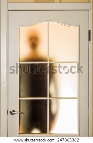 Silhouette of an unknown man in black seen through a closed glass door, like a ghost or an alien
