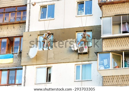 Kiev, Ukraine - June 30, 2015:  Facade plasterers build the  external thermal insulation of an apartment sitting on their swing, suspended in midair