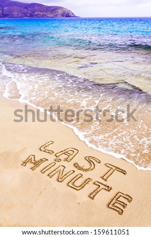 Last Minute written on sand, with waves in background, vacation concept