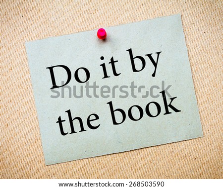 DO IT BY THE BOOK Message. Recycled paper note pinned on cork board. Concept Image