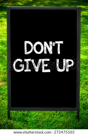 DON\'T GIVE UP  message on sidewalk blackboard sign against green grass background. Copy Space available. Concept image