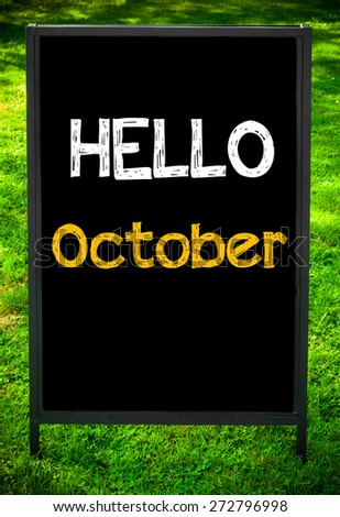 HELLO OCTOBER  message on sidewalk blackboard sign against green grass background. Copy Space available. Concept image