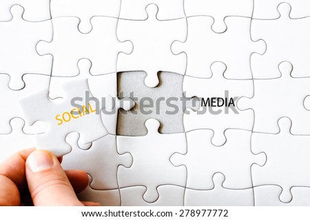 Hand with missing jigsaw puzzle piece completing the wordS SOCIAL MEDIA. Business concept image for completing the final puzzle piece.