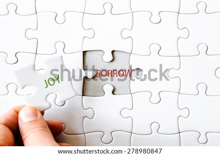 Hand with missing jigsaw puzzle piece. Word JOY, covering  the text SORROW. Business concept image for completing the final puzzle piece.