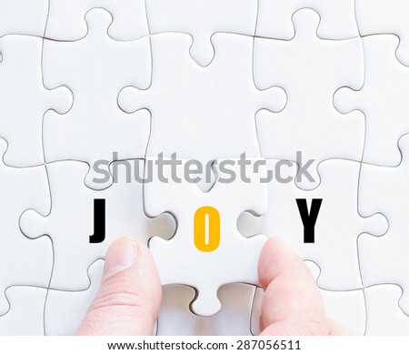 Hand of a business man completing the puzzle with the last missing piece.Concept image of puzzle board with motivational word JOY
