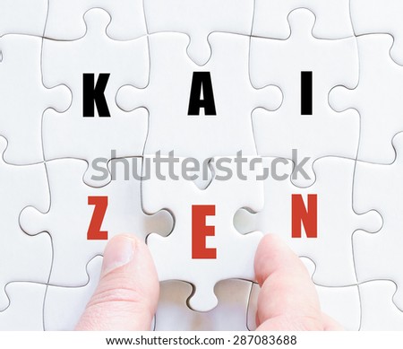 Hand of a business man completing the puzzle with the last missing piece.Concept image of puzzle board with business word KAIZEN