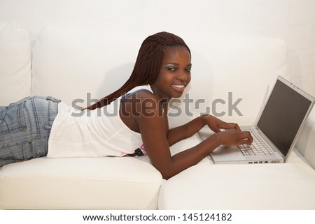 young african woman typing on computer laying on couch
