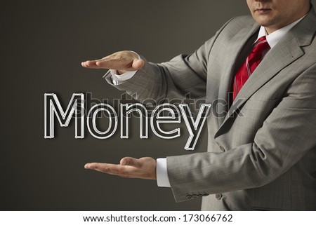 Young businessman in a black suit and tie holding a word Money on a gray background. Concept of problem and solution. Slide presentation.