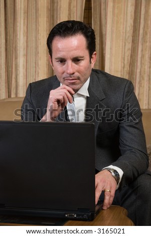 Man in business suit sitting on beige leather sofa looking at a laptop computer
