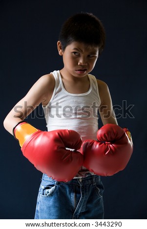 Young asian boy with mean expression wearing red boxing gloves standing on black background