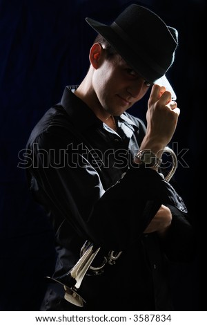 Handsome young man holding a trumpet wearing a black hat on black
