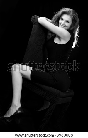Whole body of a beautiful red hair woman in black sitting on a black chair on black