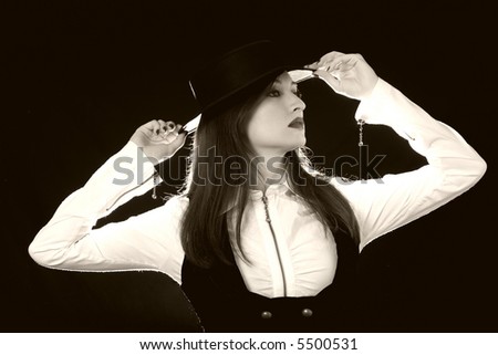 Attractive long haired brunette woman in black fedora style hat with black vest over white standing in profile on black