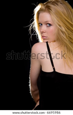 Attractive woman with long blond hair and blue eyes with serious expression wearing black looking over bare shoulder