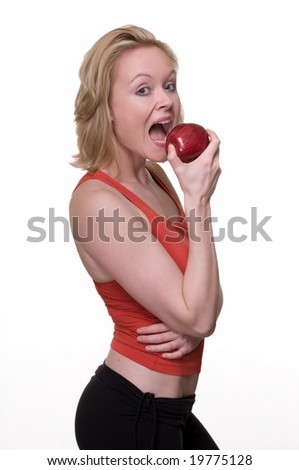 Attractive blond hair woman in red and black workout attire taking a bite of an apple standing over white