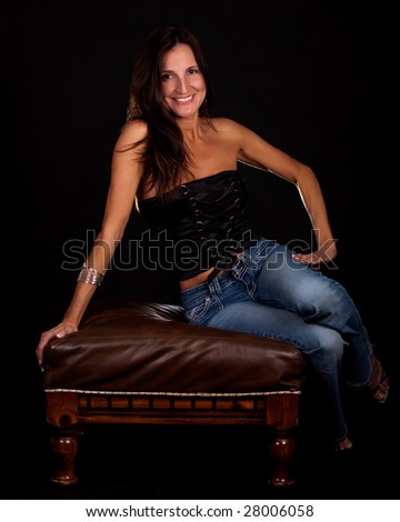 Attractive brunette woman on black wearing black sleeveless sexy top and jeans smiling sitting
