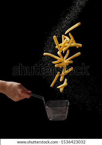 French fries - fried potatoes flying out of basket in hand, fly fastfood isolated on black background