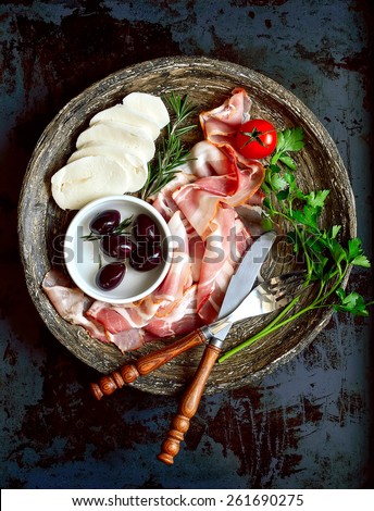 Sliced bacon on a dish with mozzarella, marinated olives and herbs