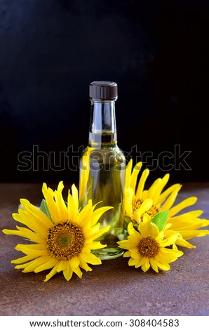Sunflower oil in a glass bottle decorated with fresh sunflowers on a dark background, vertical image