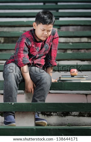 an asian boy sitting on a green concrete bench with sad expression