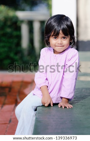 adorable smiling asian girl sitting on a concrete bench in a park