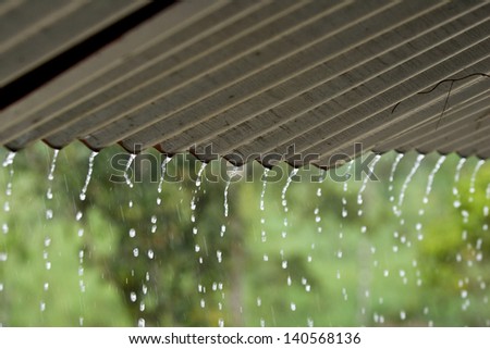 Streams of rain water pour off a corrugated roof, grey roof, green background selective focus