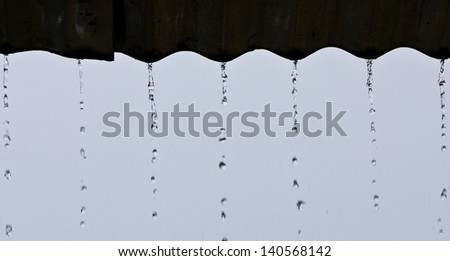 Streams of rain water pour off a corrugated roof, grey roof, green background selective focus