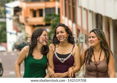 Three young Hispanic ladies sight seeing walking in the street, building in distance