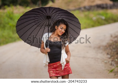 Young attractive Ecuadorian lady walking with black umbrella in the rain
