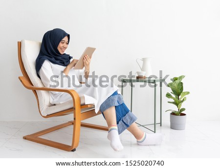Young muslim Indonesia asian woman happy on tablet casual home chair. Malay lady journalist sit Hijab girl Islam business on phone smartphone mobile online. Ramadan Malaysia family video call isolate. Imagine de stoc © 