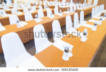 blurred image of many row of chairs set for conference, dinner or meeting event with large hall with people.