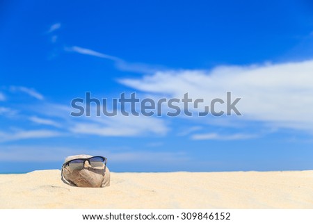 Sunglasses over coconut fruit on sandy beach under hot shiny sun light looked like a happy (tourist) man lying on the beach during holiday summer vacation on wonderful trip under bright blue sky.