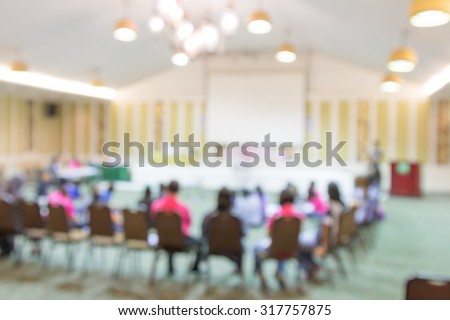 blurred image of many row of chairs set for conference, dinner or meeting event with large hall with people activity.