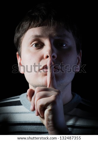 Businessman holds his finger near lips on a black background