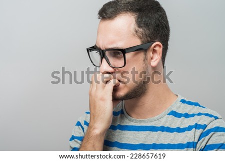 Closeup portrait of a nerdy young guy with glasses biting his nails