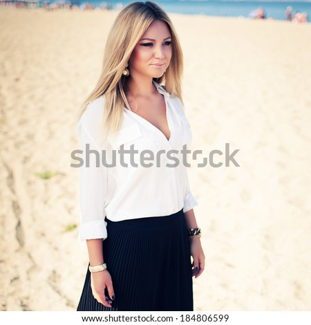 young beautiful woman blonde poses on a beach. dressed in a white shirt and a black skirt. fashion model